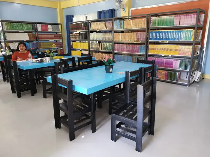 Recycled chairs at blue reading tables in front of full bookshelves in the Liloan school library